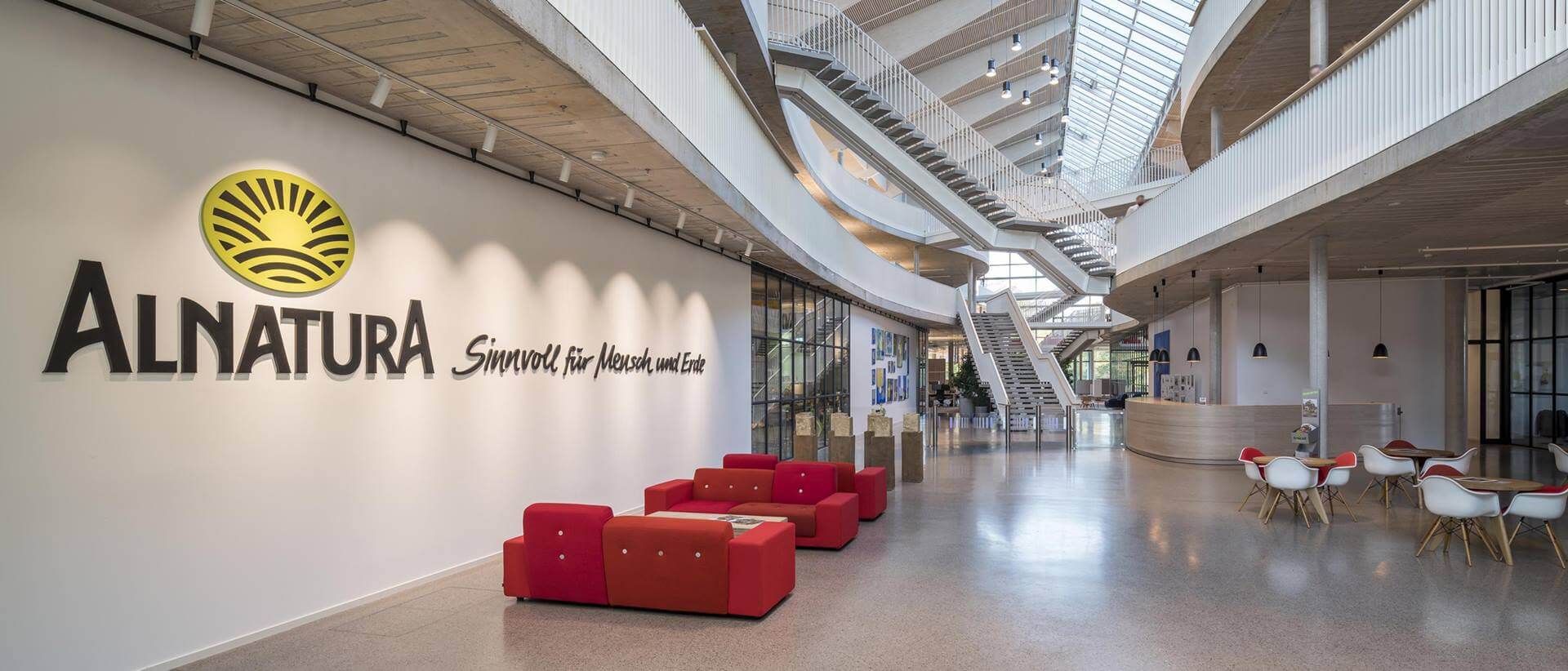 Foto des Innenraums der Alnatura Arbeitswelt vom Erdgeschoss aufgenommen. Links an der Wand ist das Alnatura zu sehen, in der Mitte der Eingangbereich und oben im Bild verschiedene Treppen und Übergänge zwischen den Ebenen.